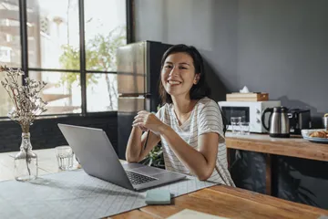 Portrait of a smiling young entrepreneur working from home on her laptop computer, looking at camera.