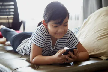 Anak perempuan menggunakan ponsel pintar. 